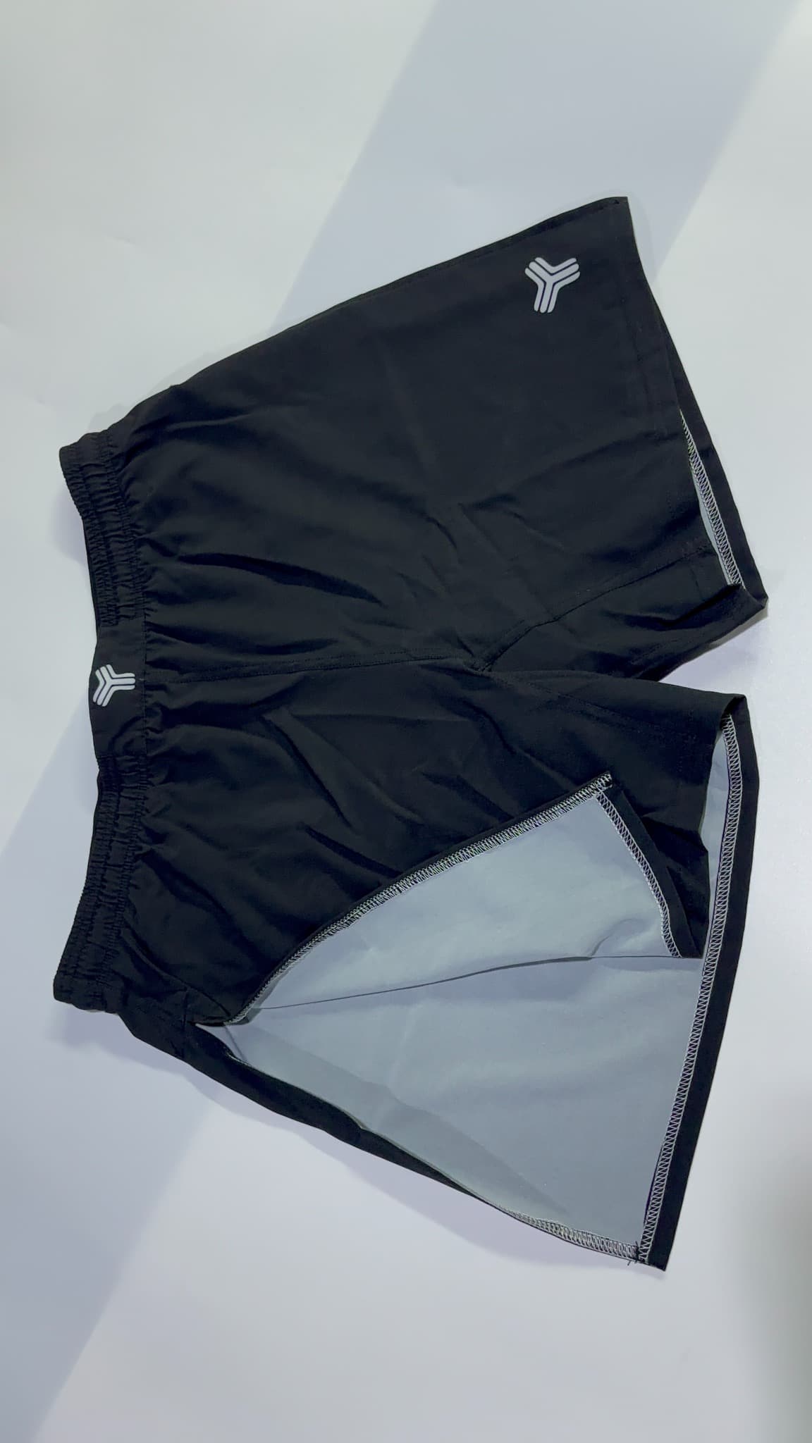 Flat-laid dark high-split shorts showing the outer shell and contrasting light fabric inside the side opening