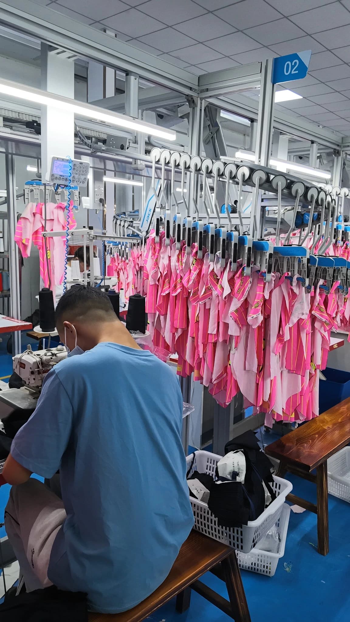 Operator working beside pink sportswear pieces suspended on the overhead hanging line