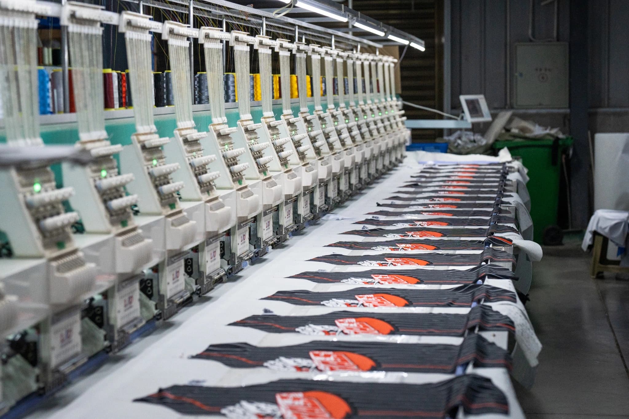 Repeated dark garment panels laid out along TONTON multi-head embroidery equipment