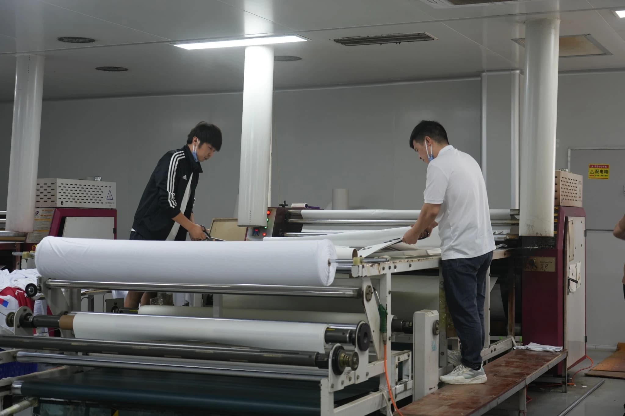 Workers preparing fabric and transfer paper at TONTON's rotary heat transfer machine
