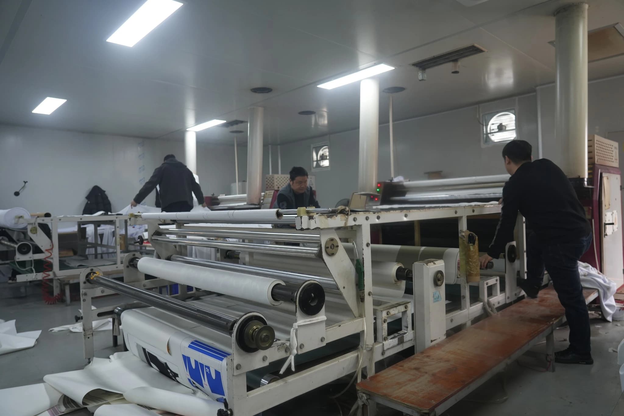 Workers preparing and feeding large fabric and transfer-paper rolls at TONTON's rotary heat transfer workstation