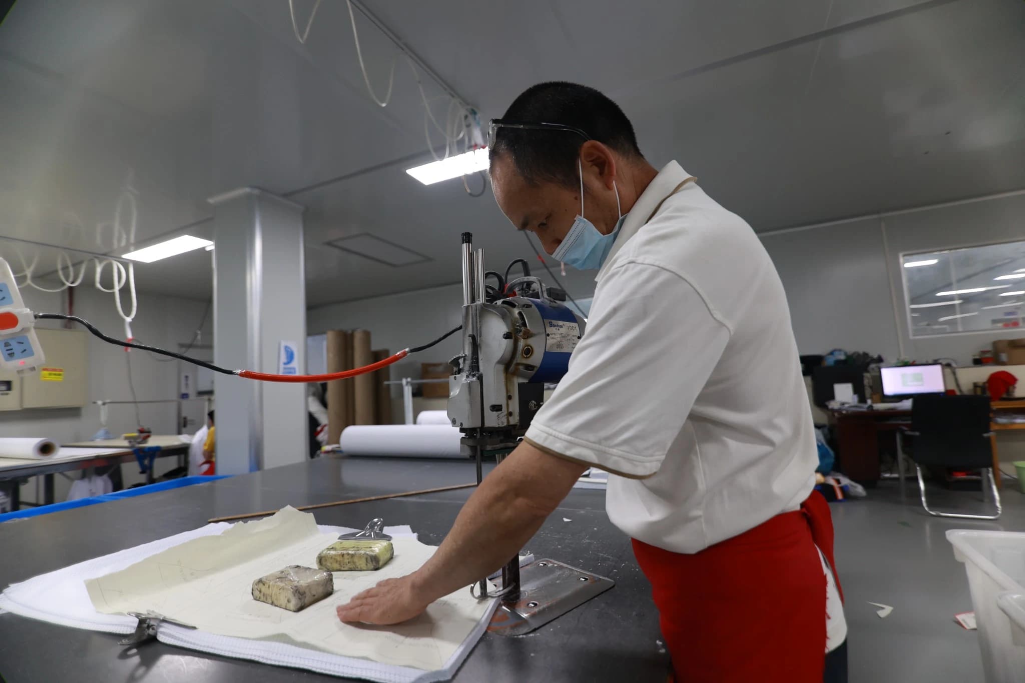 Worker guiding an electric fabric cutter alongside prepared fabric layers at TONTON