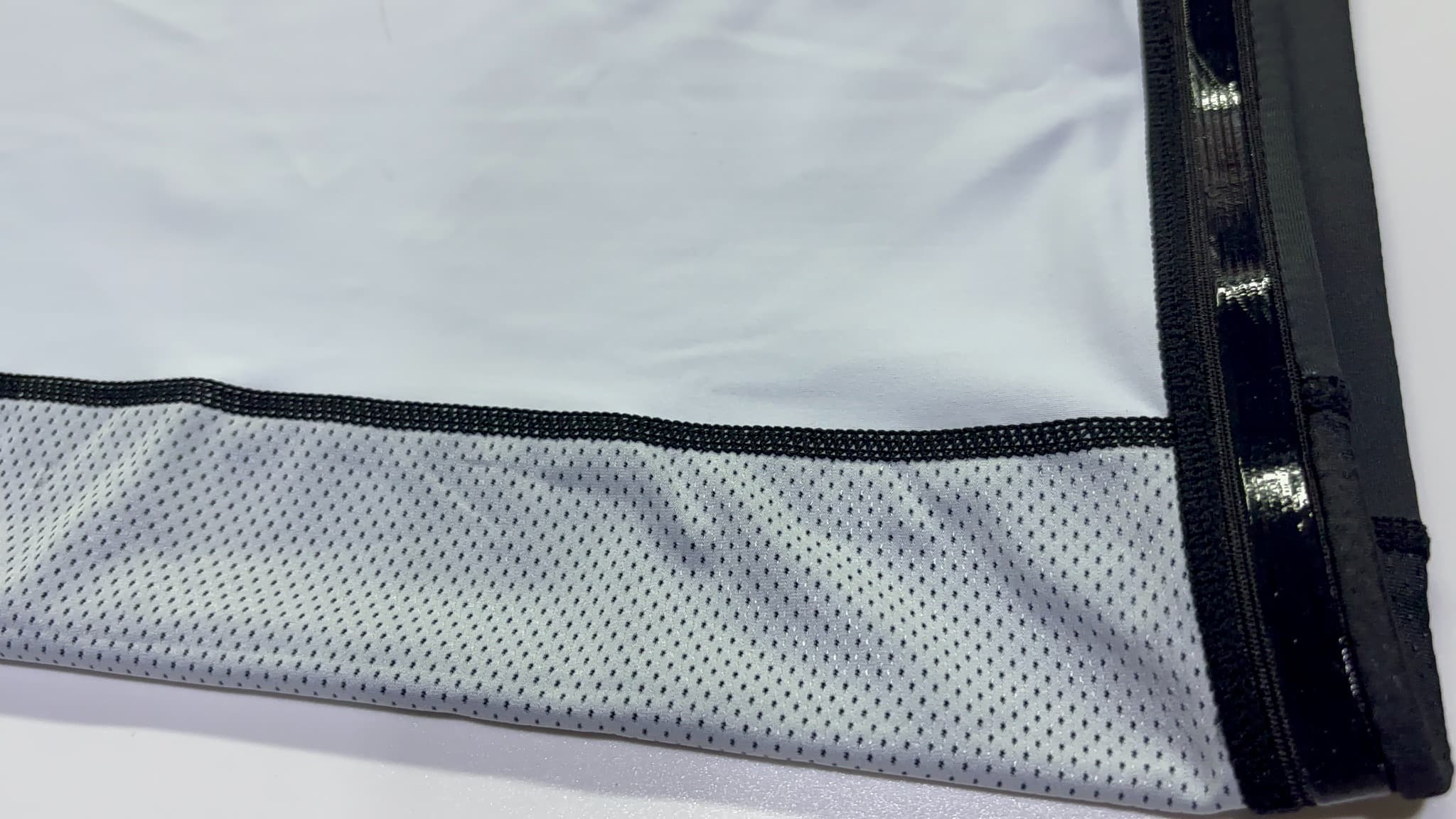 Actual supplied close-up of a light mesh panel joining dense fabric with a dark stitched seam