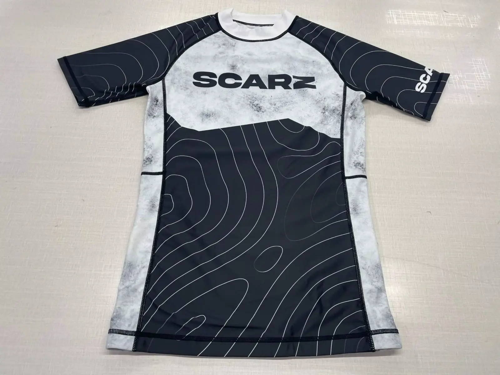 Customer-supplied front photograph of a finished black and white Athleta long-sleeve custom Rash Guard with contour-line graphics